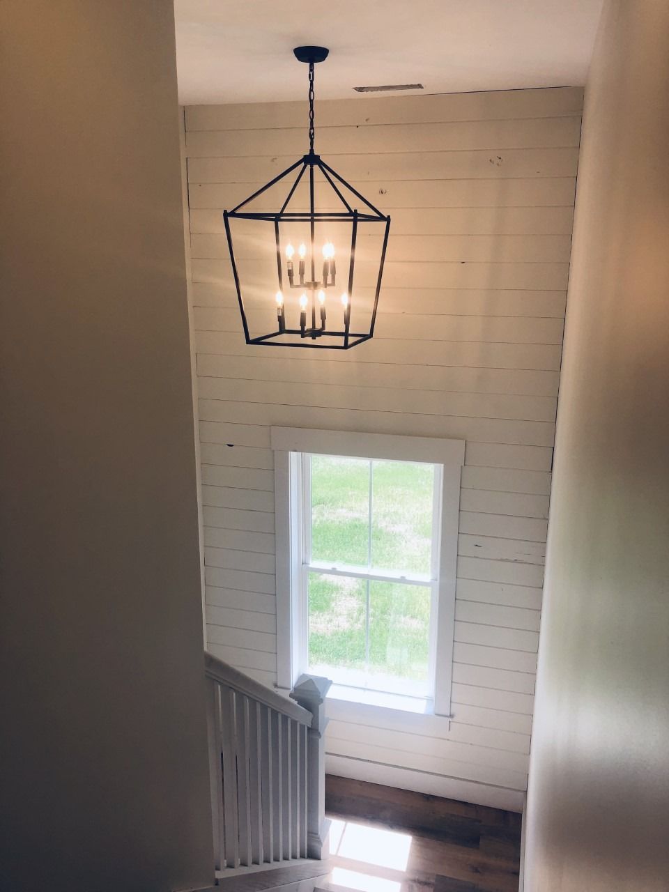 Stairwell with white wood paneled wall, chandelier, window, and white banister.
