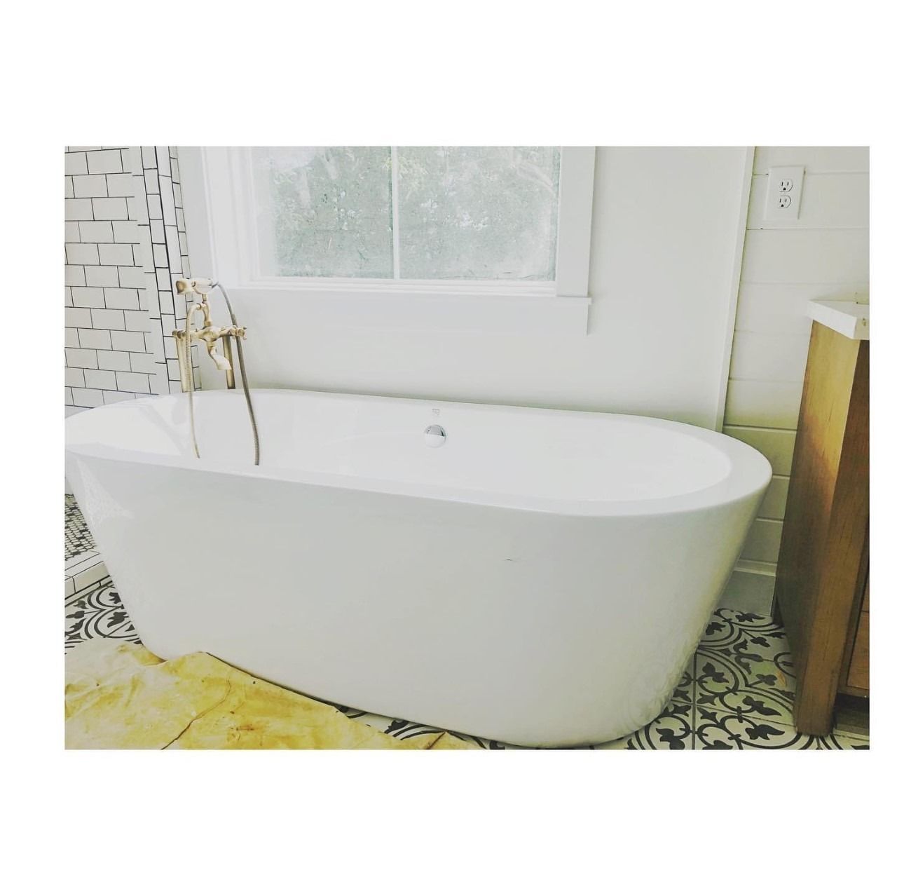 White freestanding bathtub in a bathroom, with a window behind it.