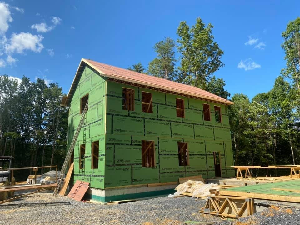 Two-story house under construction, green sheathing, unfinished roof, clear blue sky.