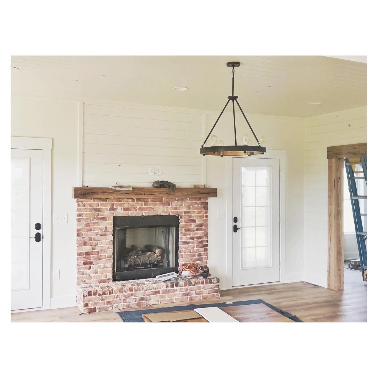 Fireplace with exposed brick, wooden mantel, and a chandelier, between white doors.