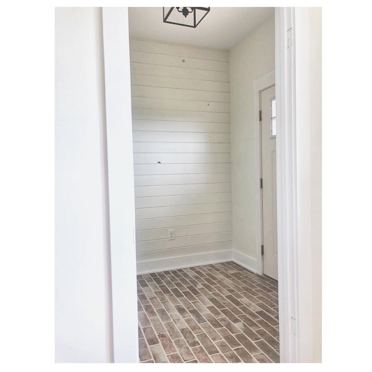 Entryway with brick floor, shiplap wall, and white door.