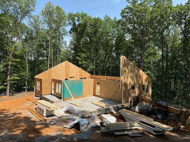 Construction site with partially built wooden house surrounded by trees.