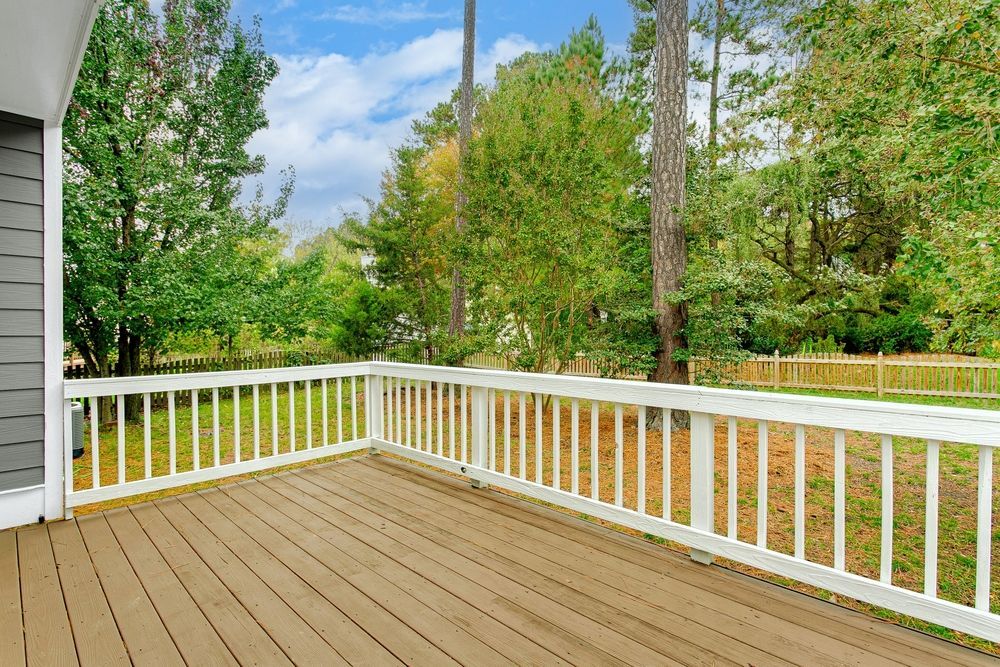 Wooden deck with white railing, overlooking a wooded backyard on a sunny day.