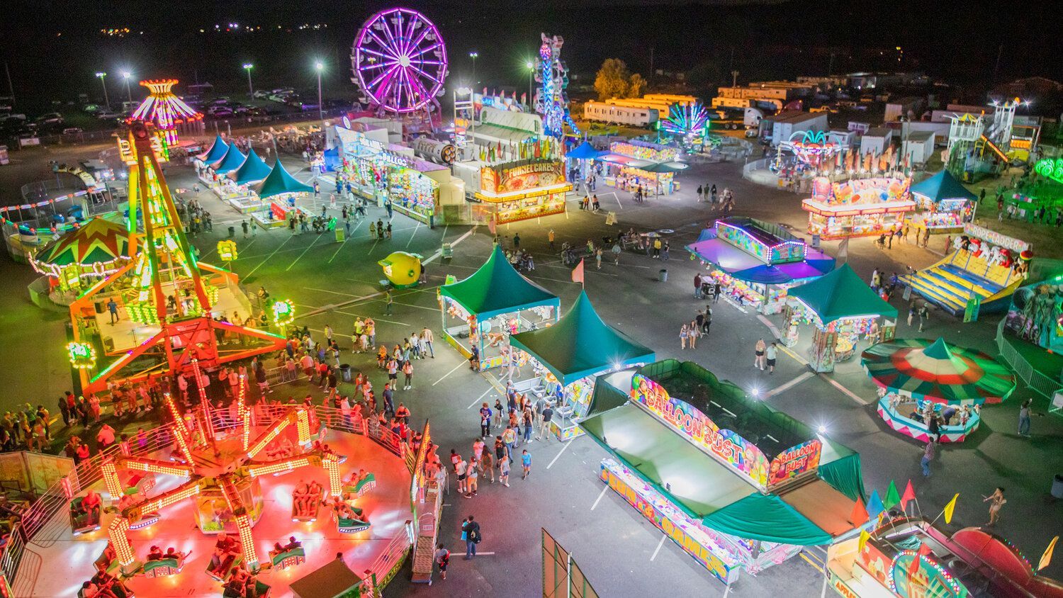 An aerial view of a carnival at night with a ferris wheel.