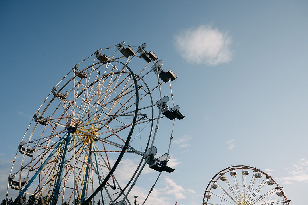 Two ferris wheels are against a blue sky with clouds.