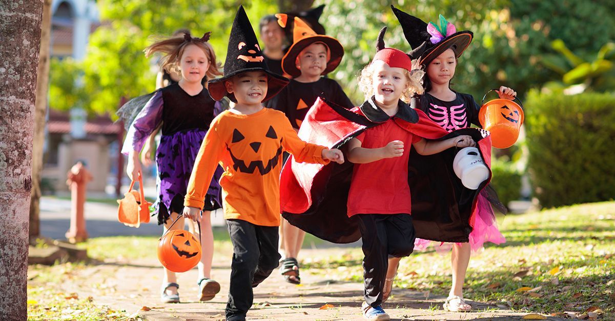 A group of children in halloween costumes are walking down a sidewalk.