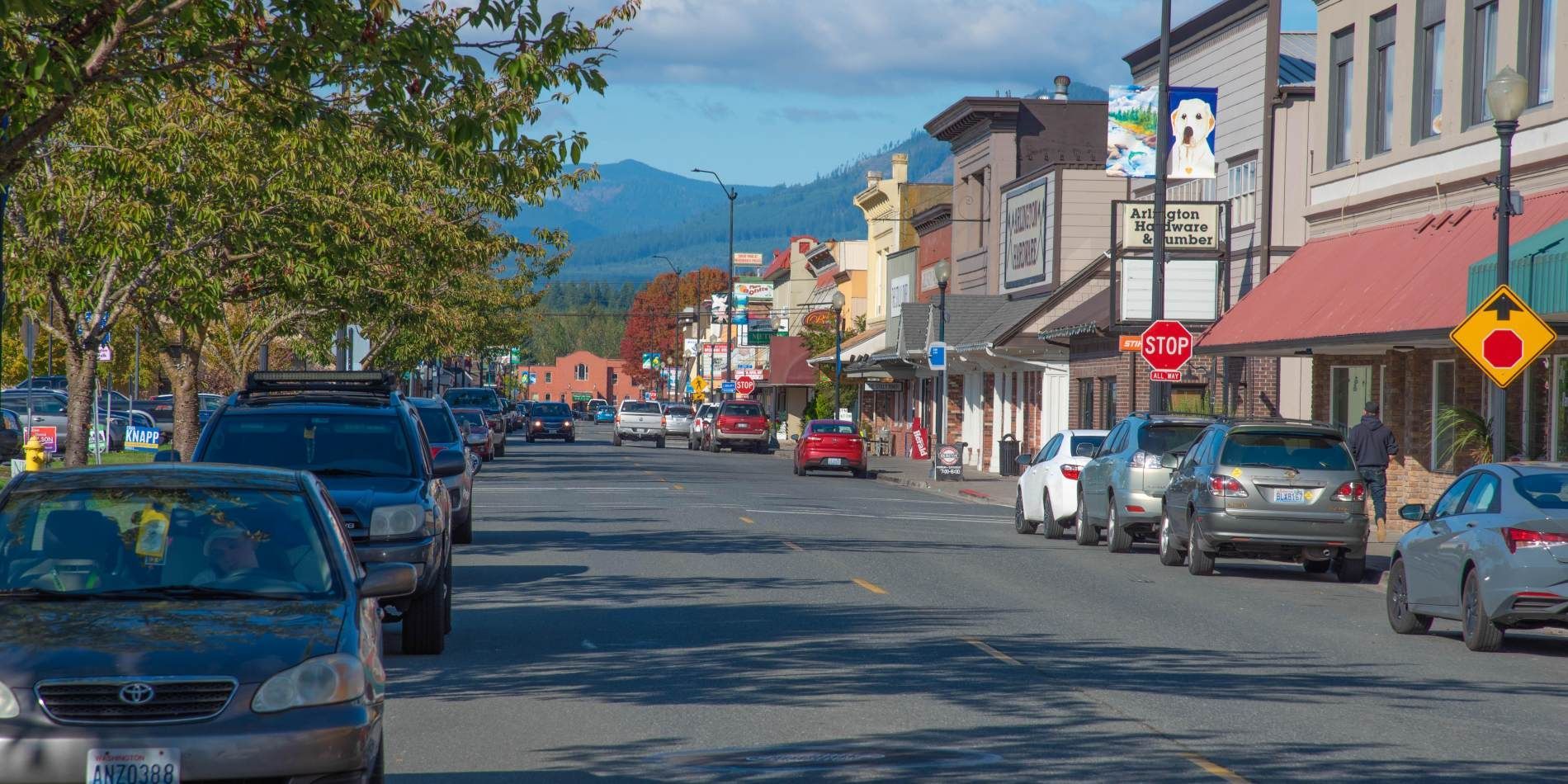 A city street with cars parked on the side of it and mountains in the background.