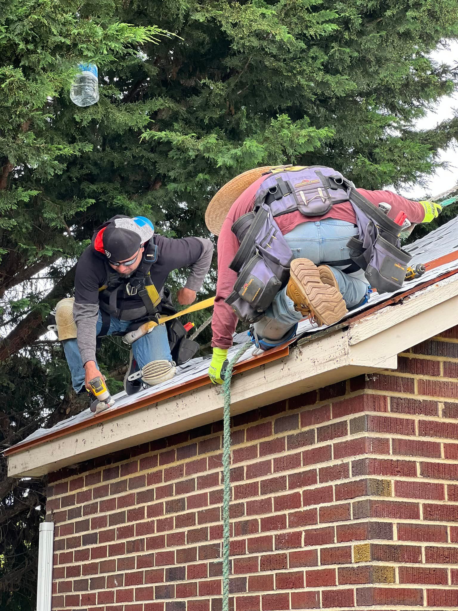 Two men are working on the roof of a brick house.
