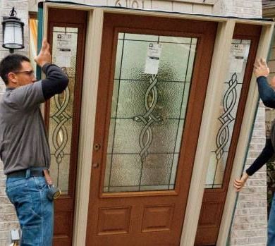 Two men are installing a stained glass door on a house.