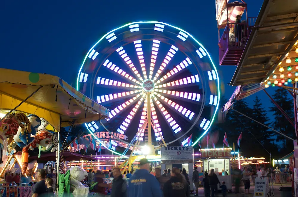 A ferris wheel is lit up at a carnival at night.