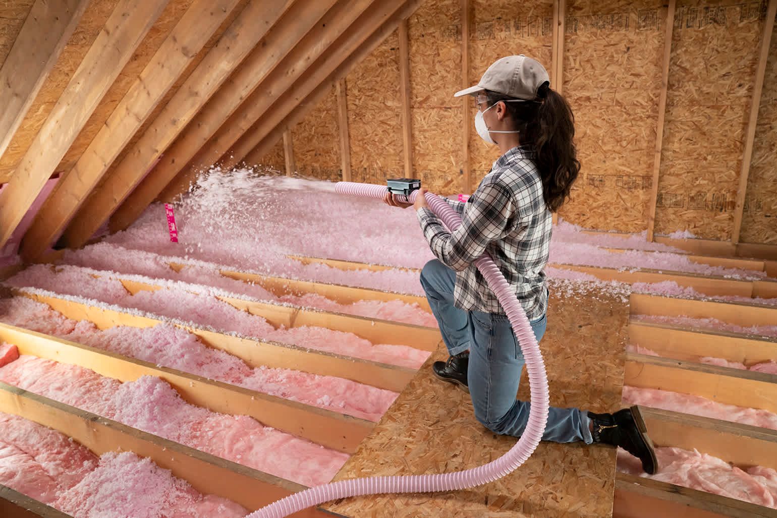 A woman is blowing insulation into the attic of a house.