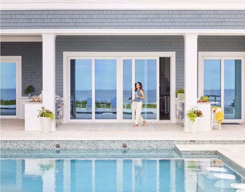A woman is standing in front of a house next to a swimming pool.