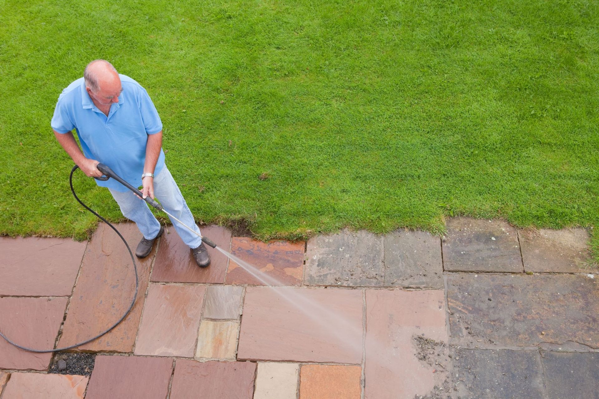 A man is using a high pressure washer to clean a patio.