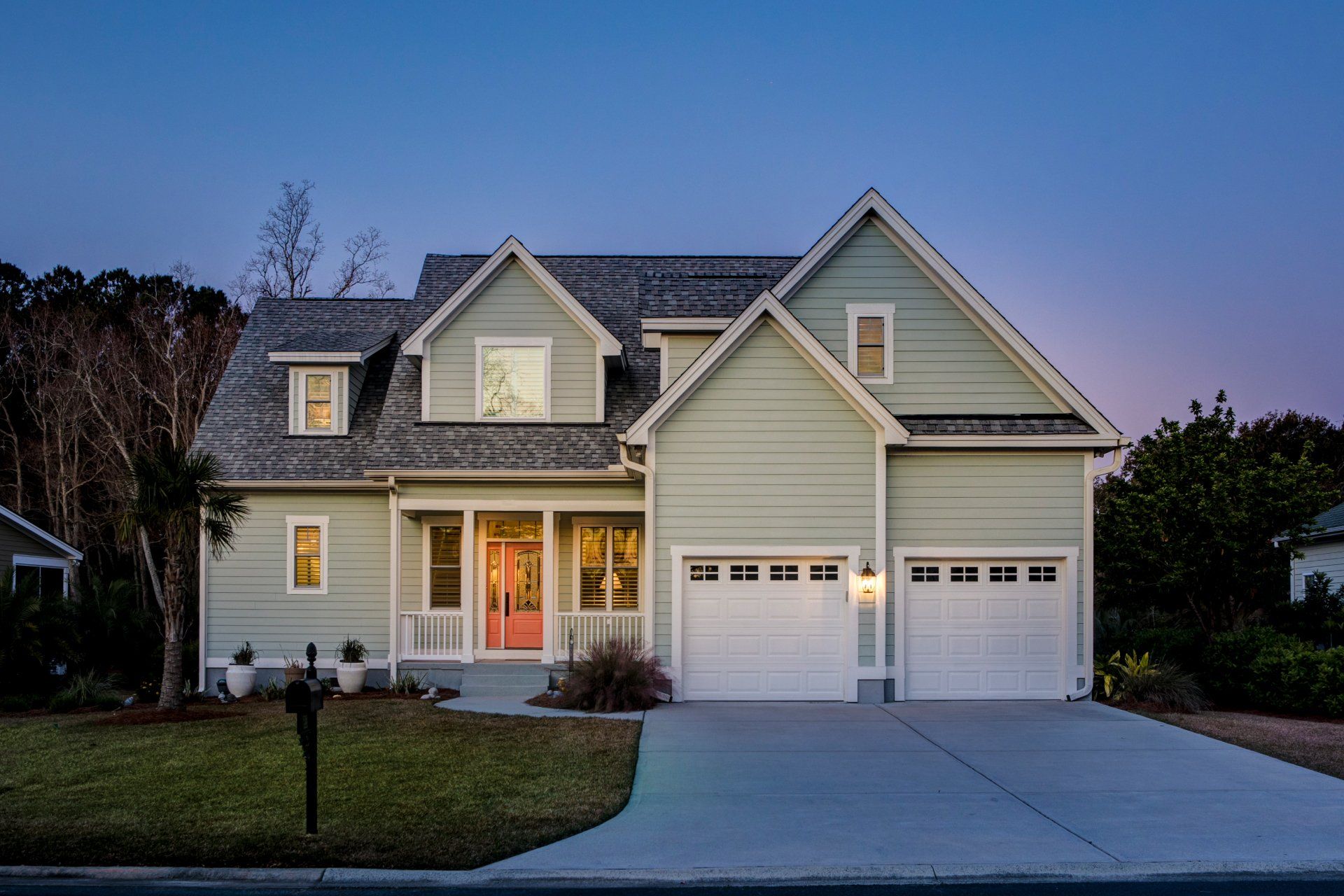 A large green house with a white garage door and a red door.