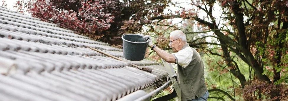 A man is cleaning a gutter on a roof with a bucket.