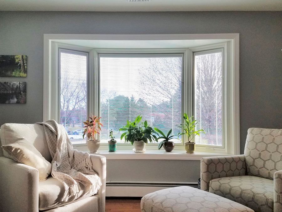 A living room with a couch , chair and ottoman in front of a bay window.