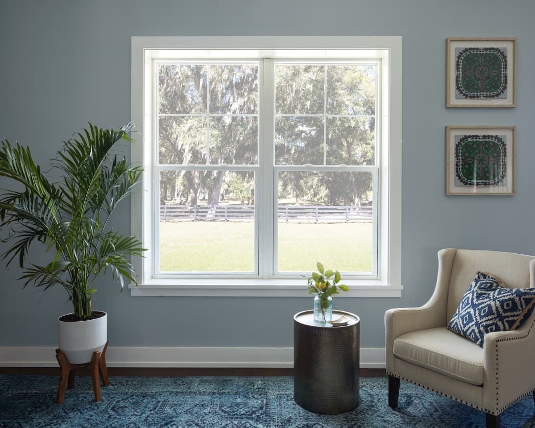 A living room with a chair , table , plant and window.