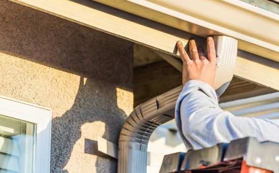 A man is installing a gutter on the side of a house.