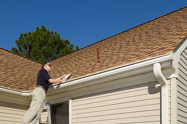 A man is standing on a ladder looking at the roof of a house.