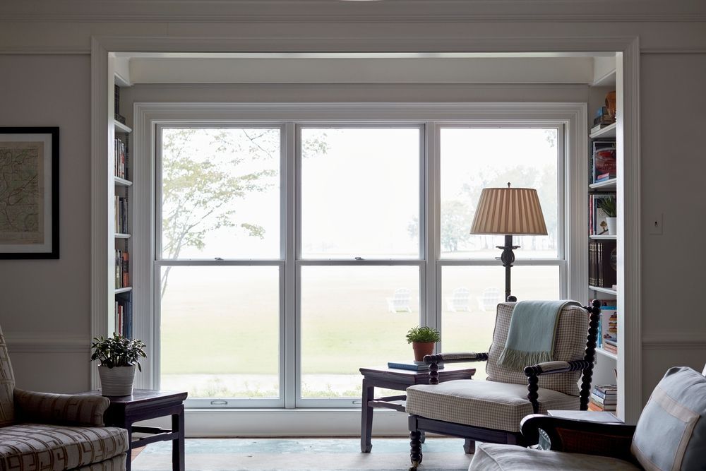 A living room with a couch , chair , lamp and a large window.