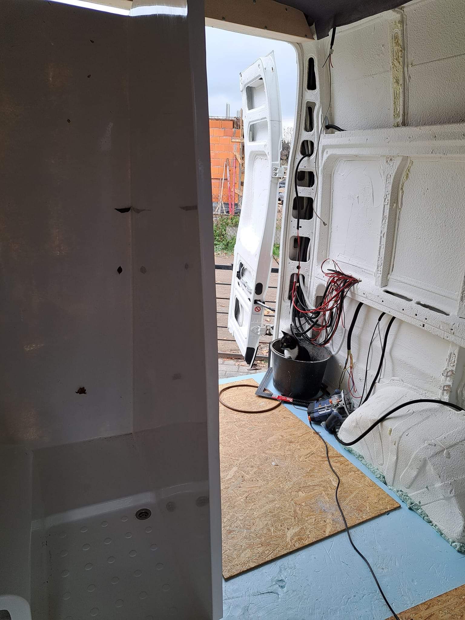Interior of a van under construction with open side door, insulation, and exposed wires.