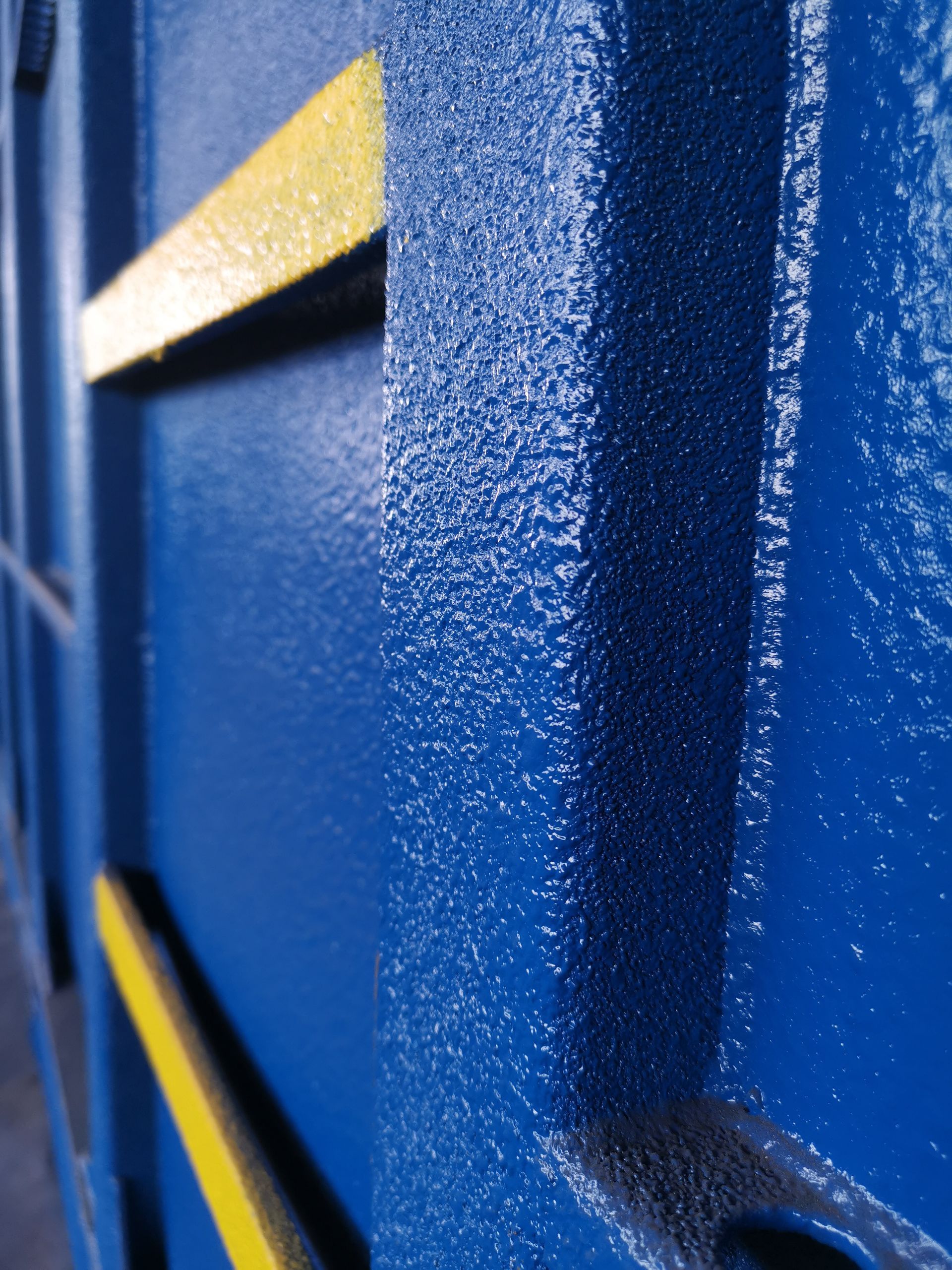 Blue metal wall with yellow stripes, textured surface.