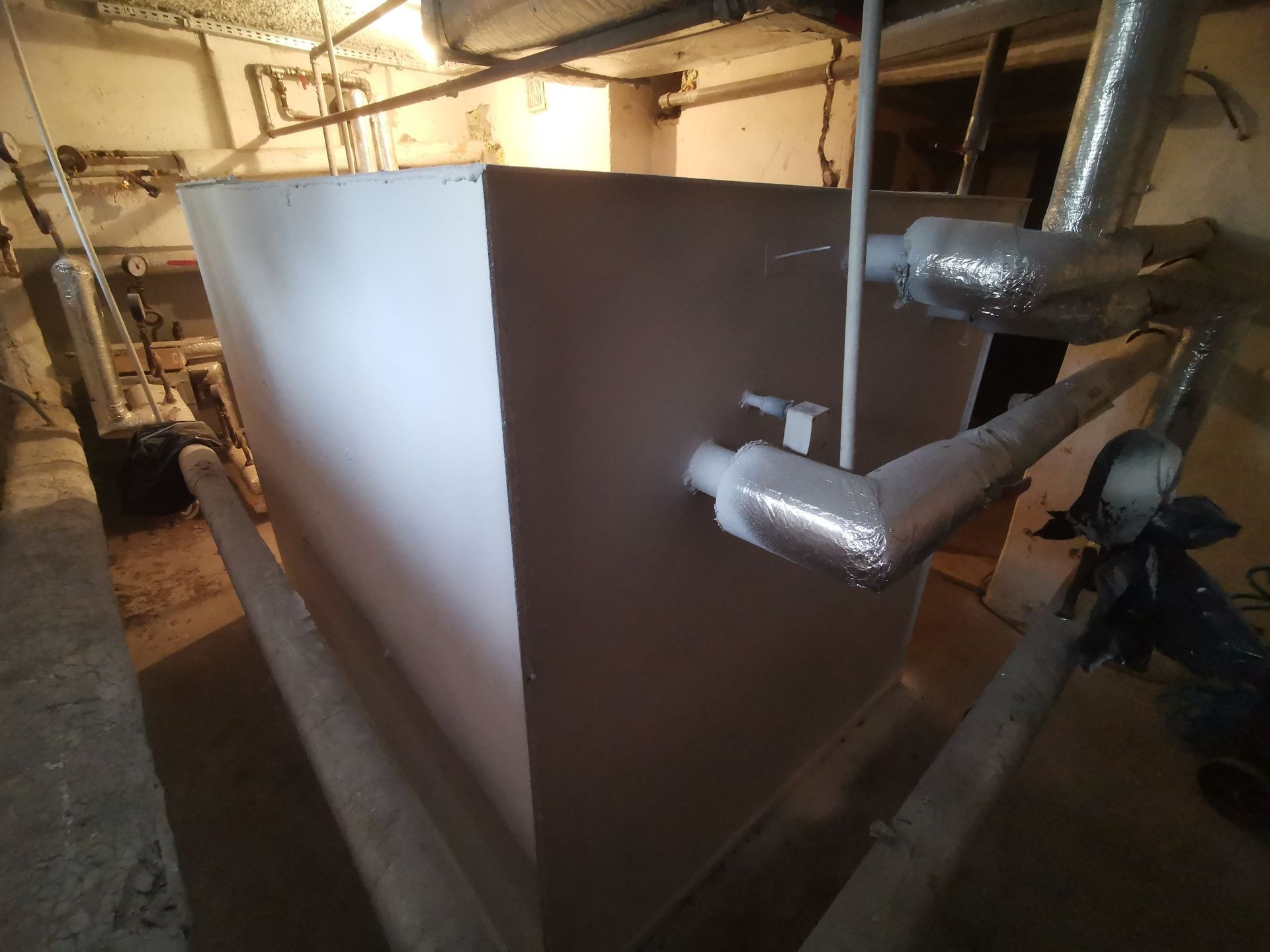 Large, white, rectangular tank with pipes in a utility room.