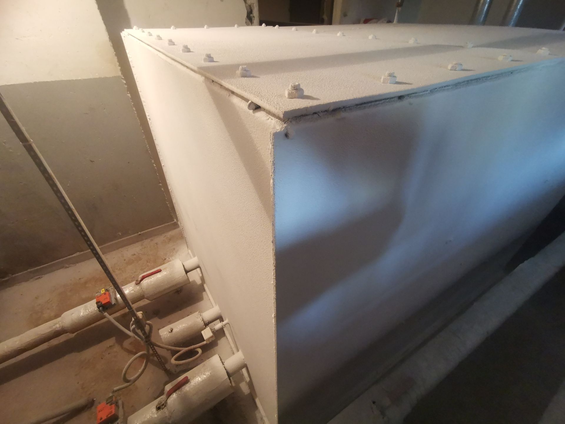 Large white tank in a room with pipes and valves, corner view.