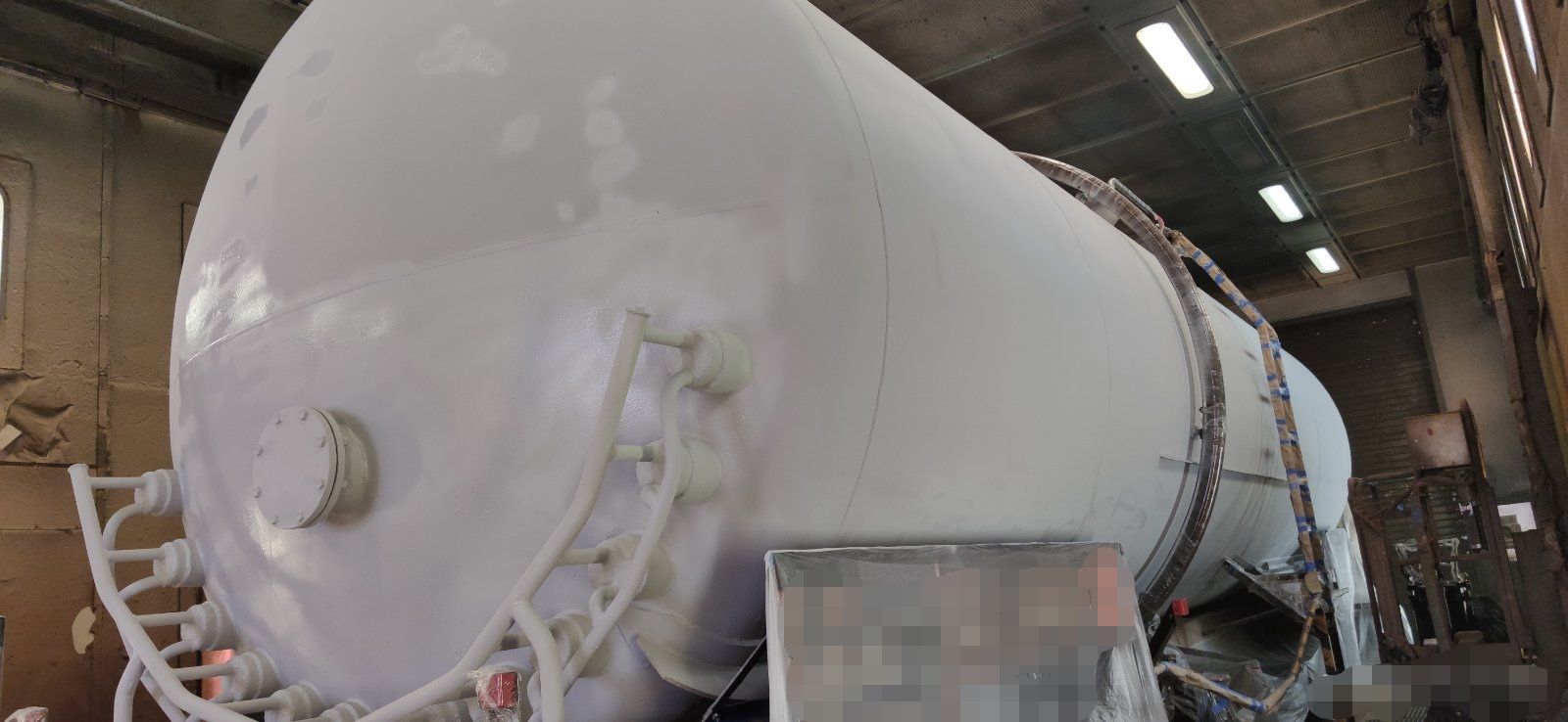 White cylindrical tank in a workshop, with supporting structure and pipes.