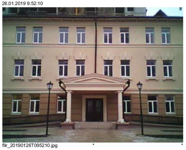 Beige building with white-framed windows and columns. Entrance with canopy, two street lamps, gray pathway.