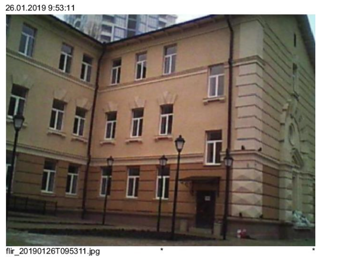 Three-story building with multiple windows, beige and light-brown facade, street lamps in front.