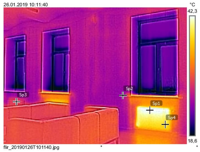 Thermal image of a room with windows and a radiator, showing heat distribution. Warmer areas appear yellow, cooler ones purple.