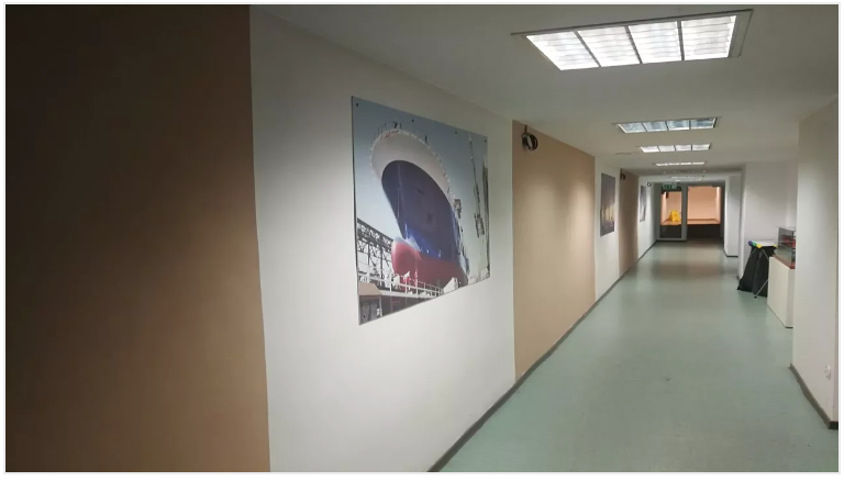 A long hallway with a photo of a ship on the wall and fluorescent lights overhead.