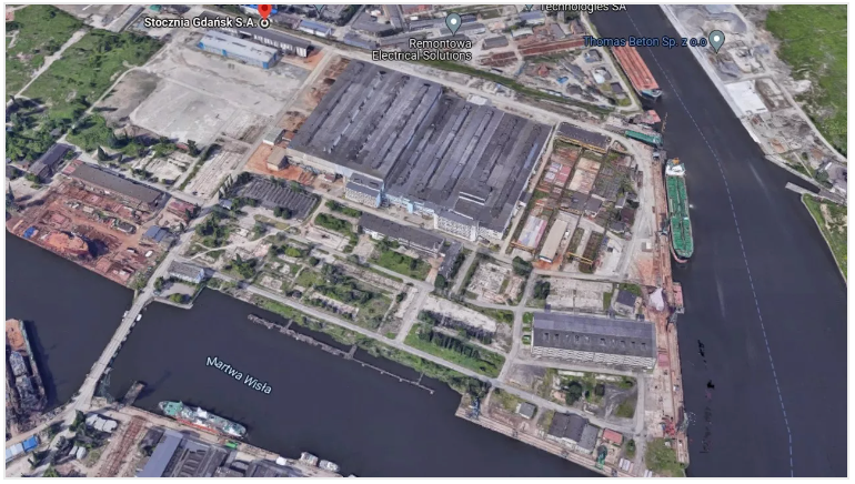 Aerial view of an industrial harbor with large buildings, docks, ships, and a waterway.