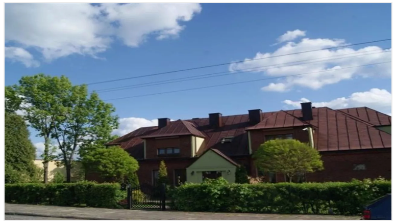A large, brown-roofed building with trees and blue sky with clouds.