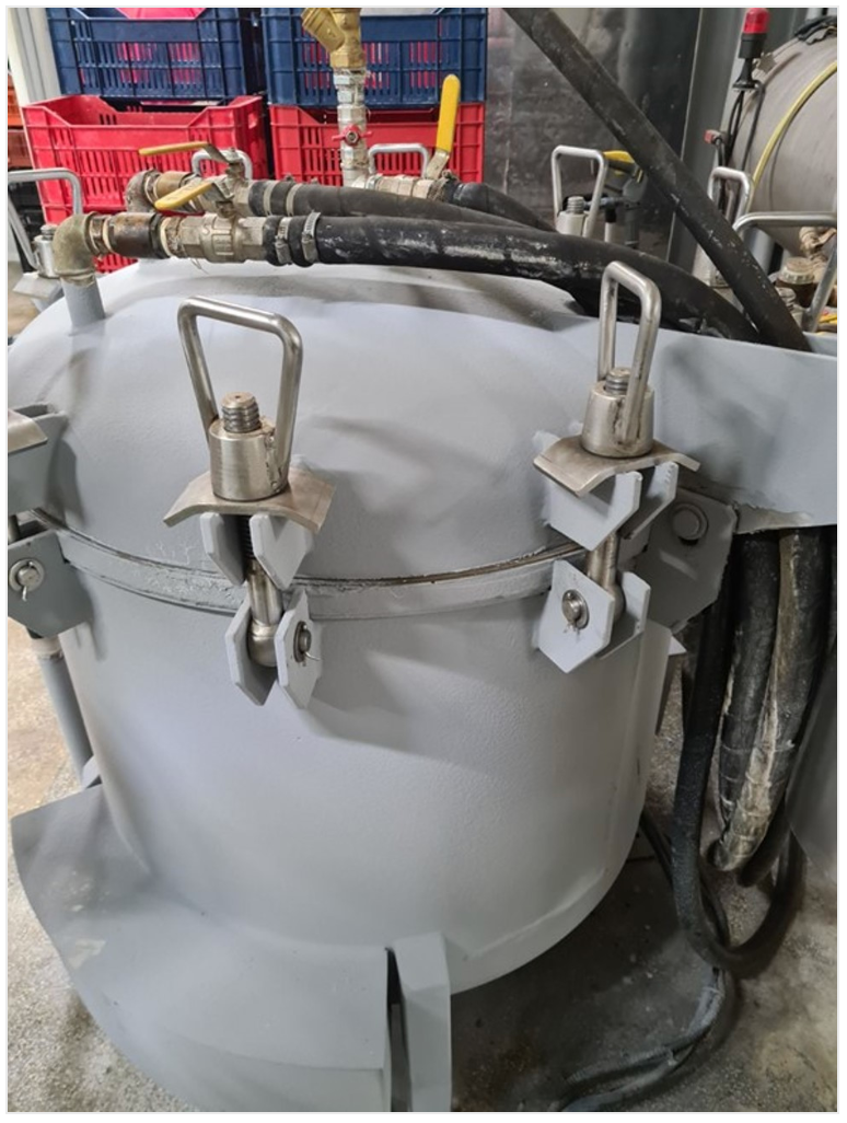 Gray pressure pot with two toggle latches and attached hoses.