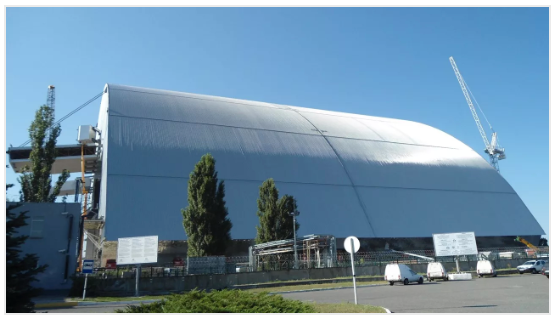 A large, silver structure over an industrial site; likely Chernobyl's New Safe Confinement.