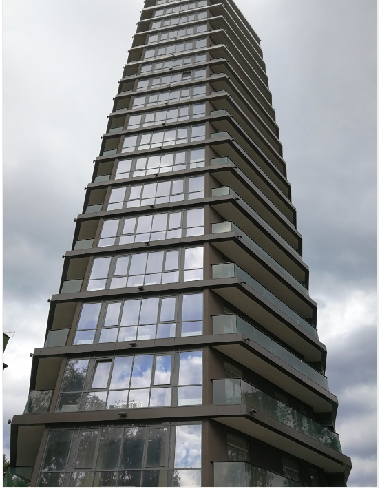Modern high-rise building with dark exterior, balconies, and reflective windows under a cloudy sky.