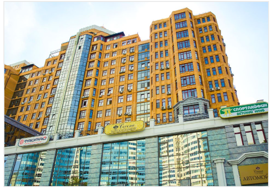 Yellow high-rise building with retail storefronts below, glass facade and multiple signs, cloudy sky.