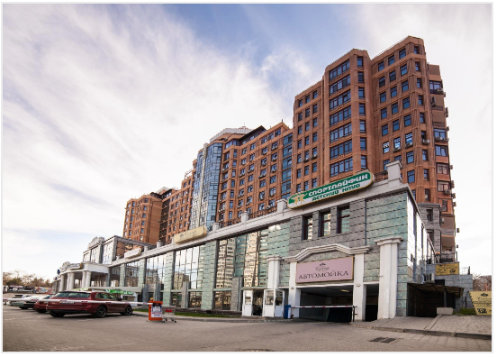 Brick and glass building with a high-rise section, parked cars, and a cloudy sky.