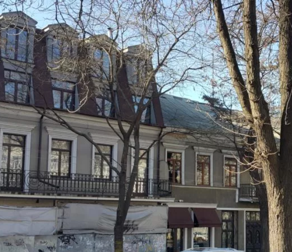Gray building with a red roof, windows, and trees in front. Sunny day.