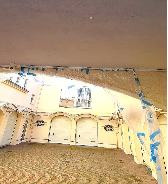 Courtyard view of a light-colored building with arched entrances, cobblestone ground, and protective plastic sheeting.