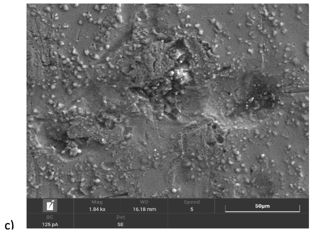 Microscopic view of a surface with grainy texture, some bumps and cracks, and many small particles.
