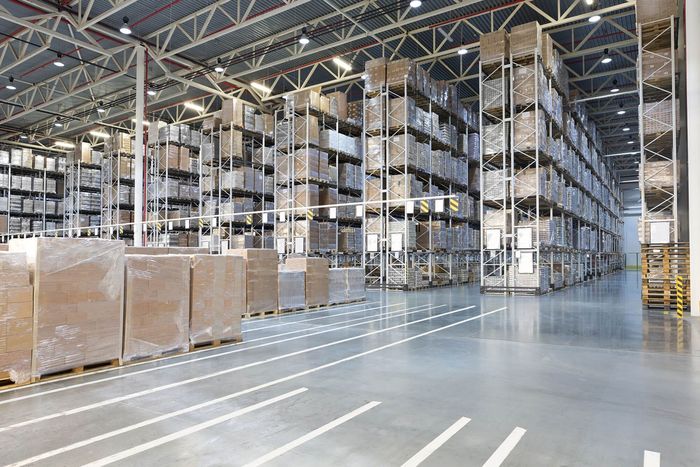 Warehouse interior with tall shelves packed with boxes, concrete floor, and overhead lighting.
