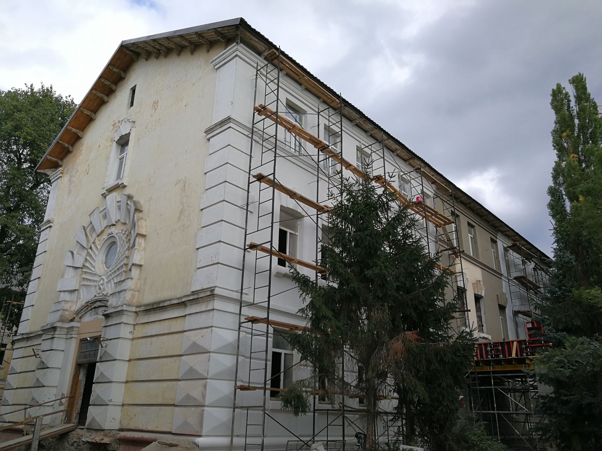 Building facade under renovation with scaffolding; gray and white; cloudy sky.