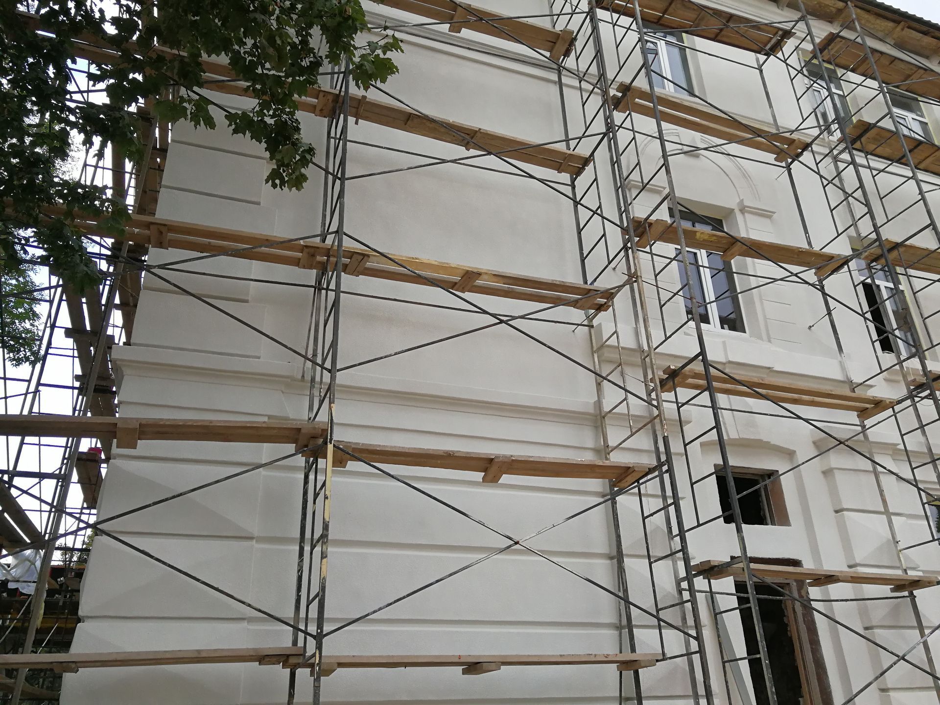 Scaffolding on a white building during renovation; windows visible.