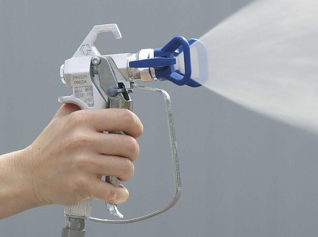 Hand holding a white and blue paint sprayer, spraying against a gray background.