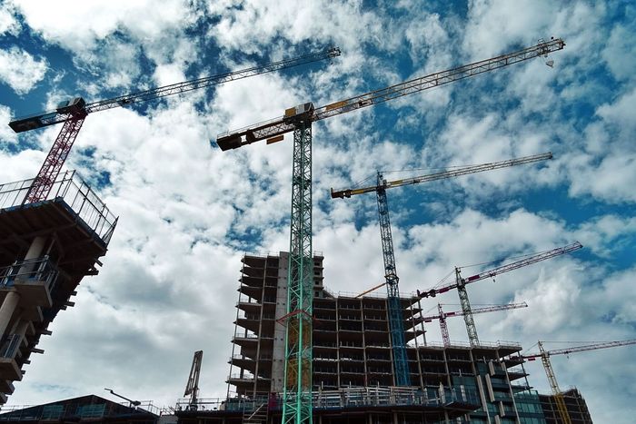 Construction site with multiple cranes against a cloudy sky.