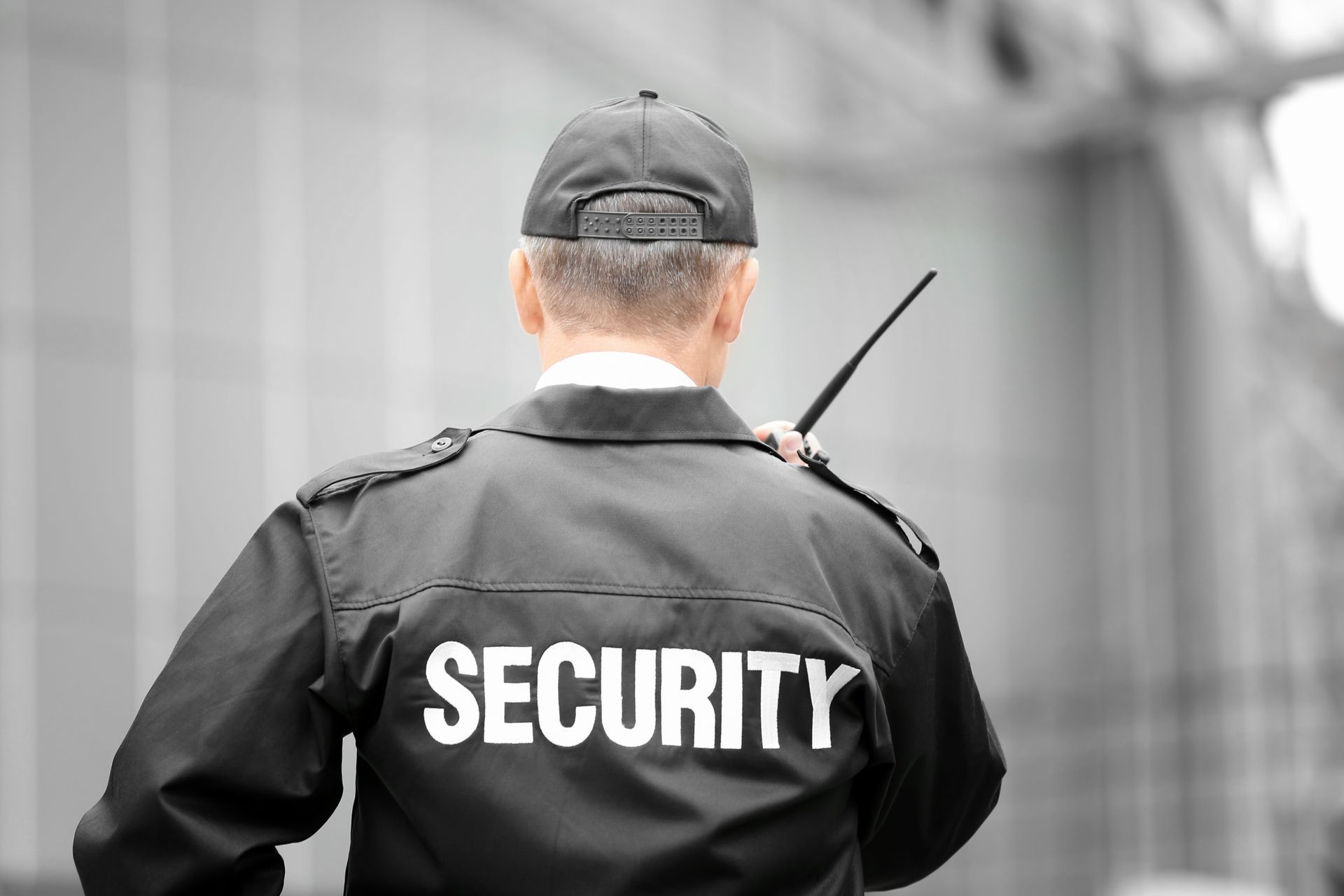Back view of a security guard wearing a jacket labeled “SECURITY” and holding a radio.
