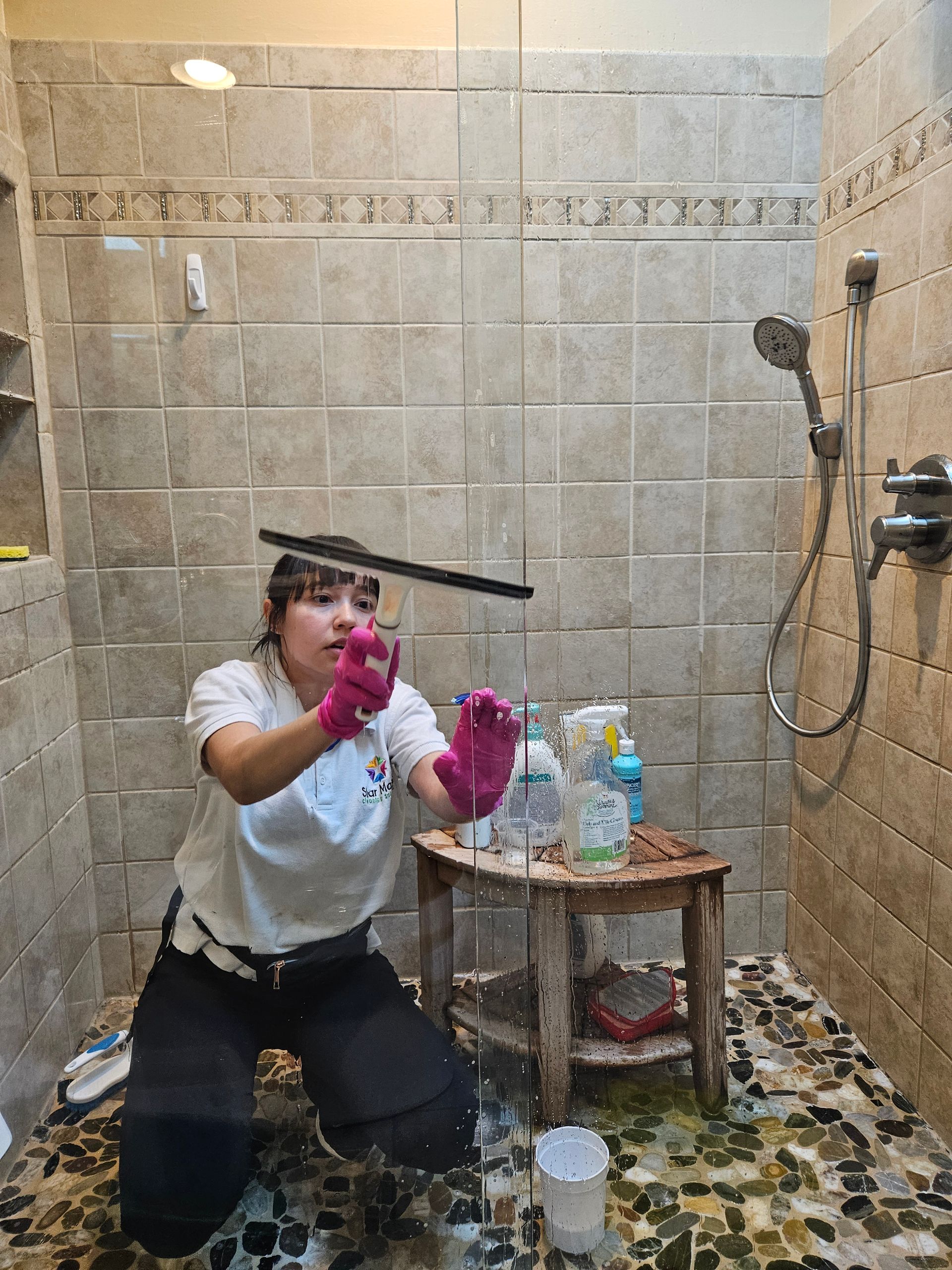 Star Maids cleaner in pink gloves squeegeeing a tiled shower door during a deep house cleaning.